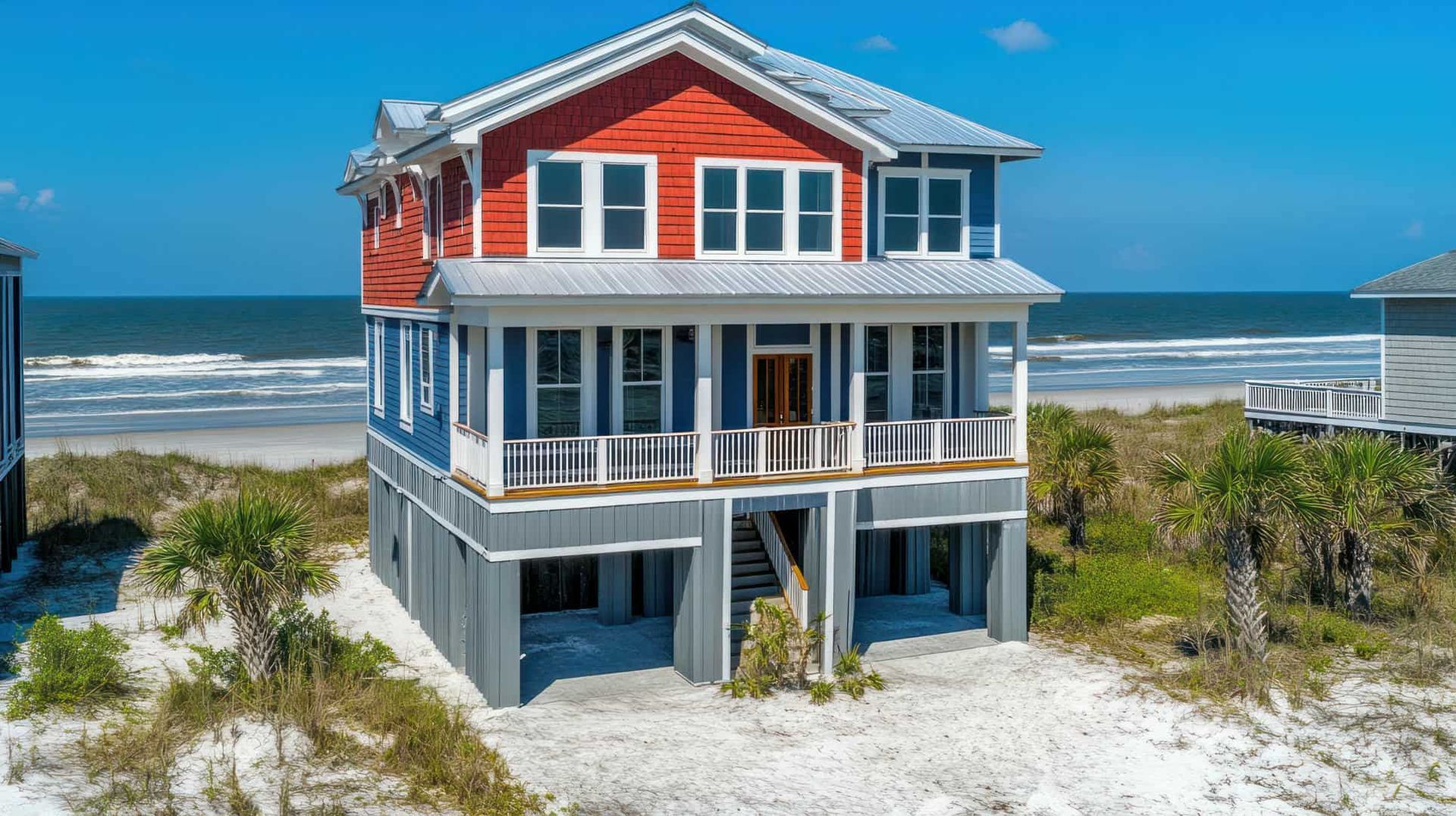 A large house is sitting on top of a sandy beach next to the ocean.