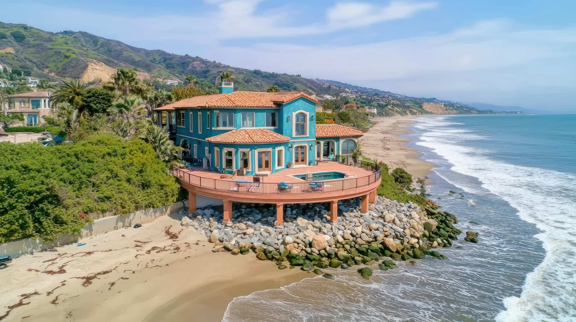 An aerial view of a large house on a cliff overlooking the ocean.