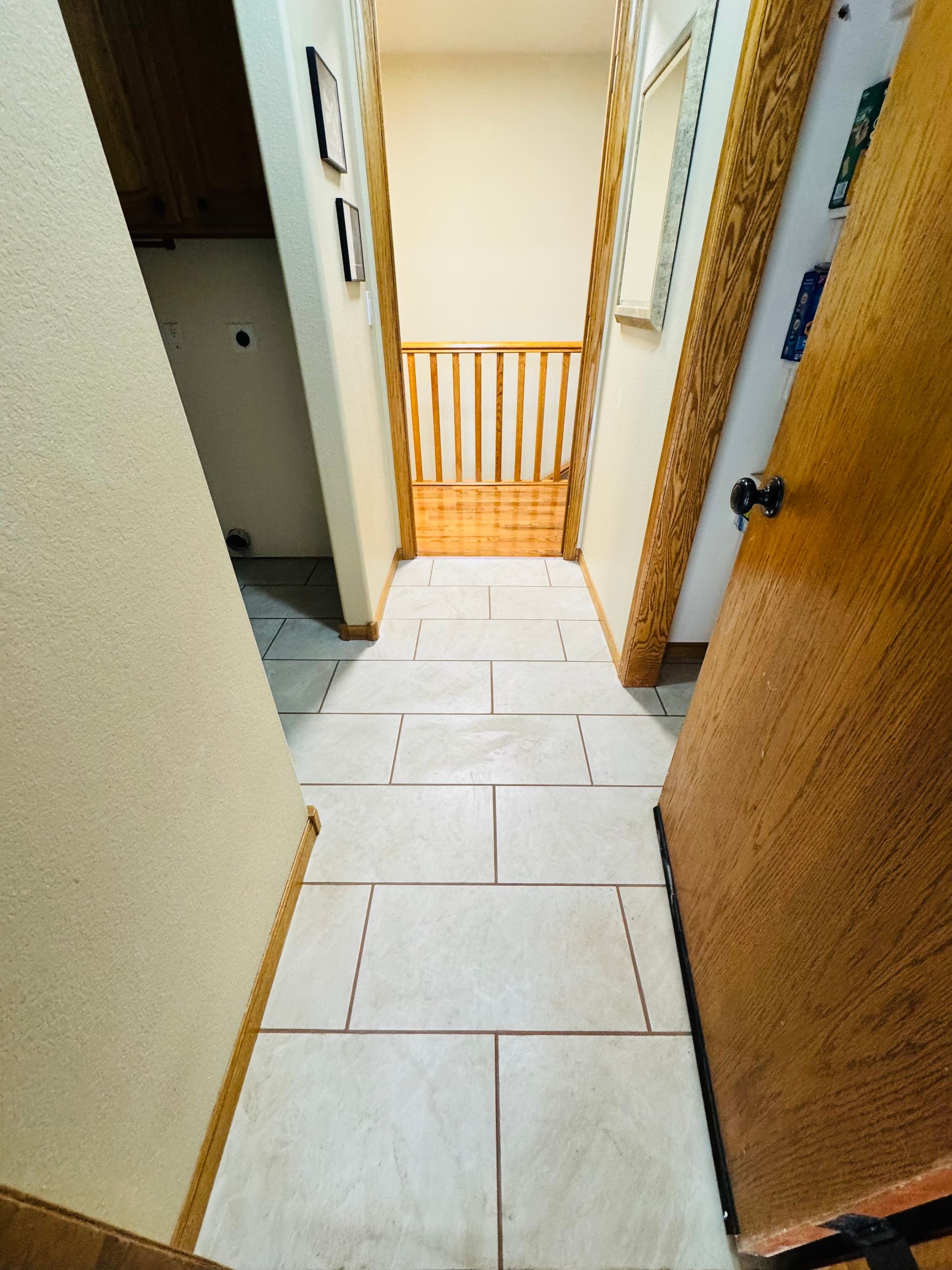 Hallway with light tile floor, baby gate, two doors, and framed artwork on the walls.