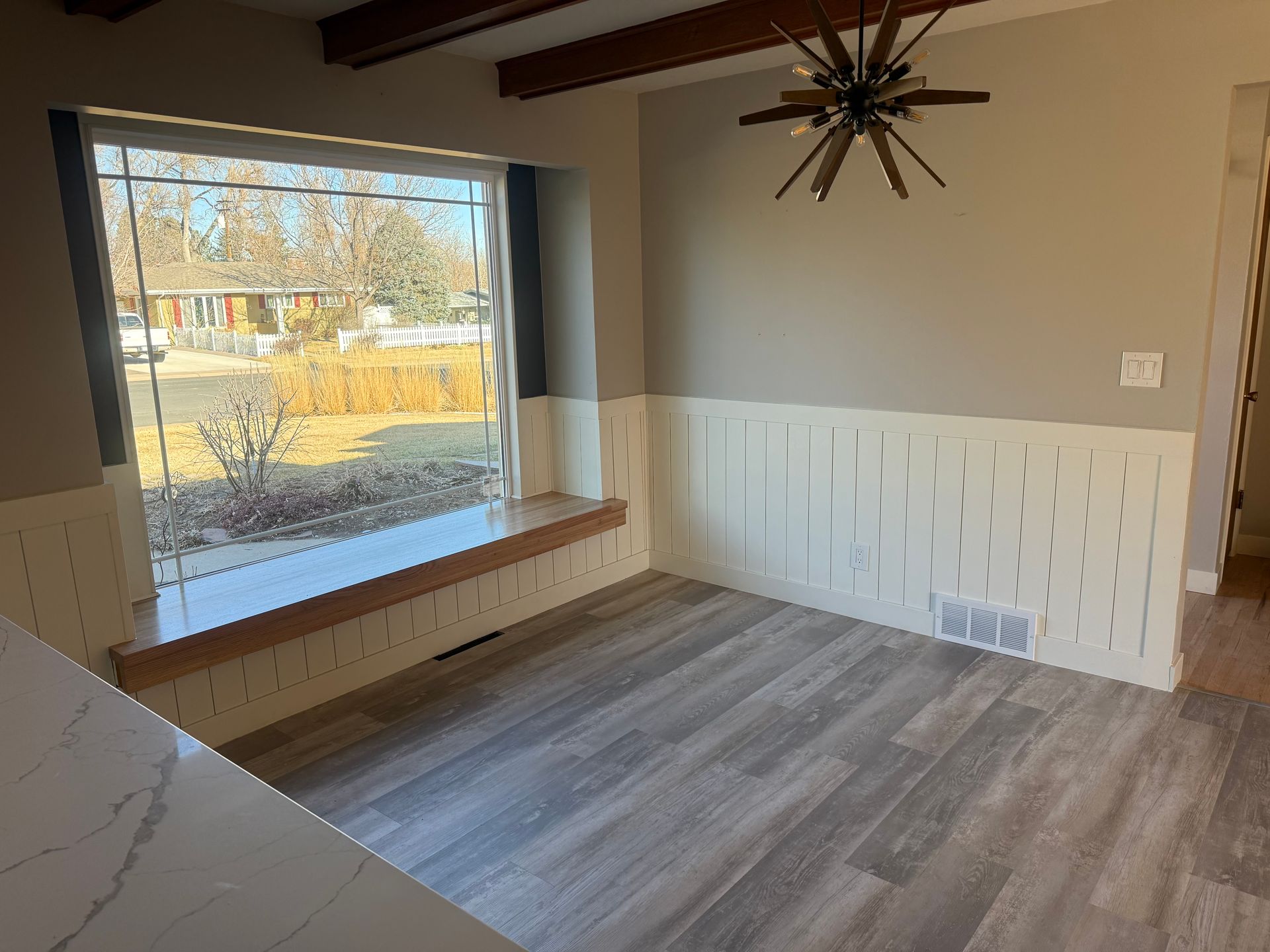 Dining room with grey wood-look floors, white wainscoting, a large window, and a hanging light fixture.