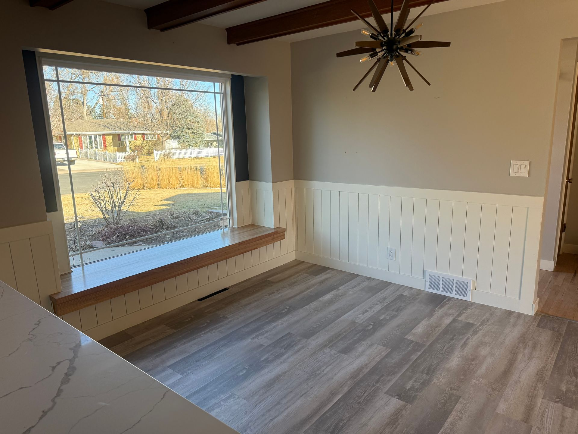 Dining room with wood beams, large window with a built-in bench, and patterned wall panels.