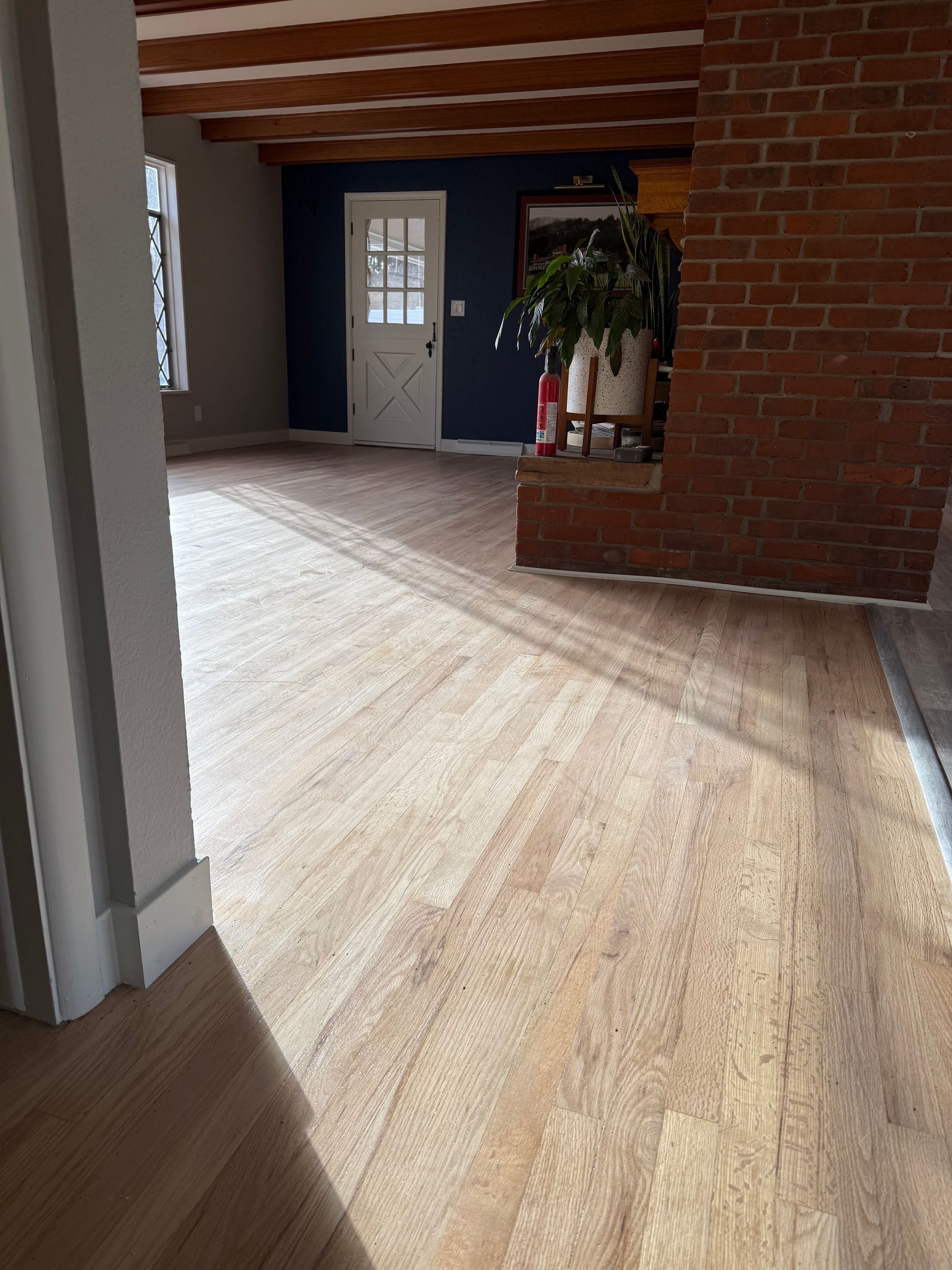 Interior view of room with wooden floor, exposed beams, brick wall, and a white door.