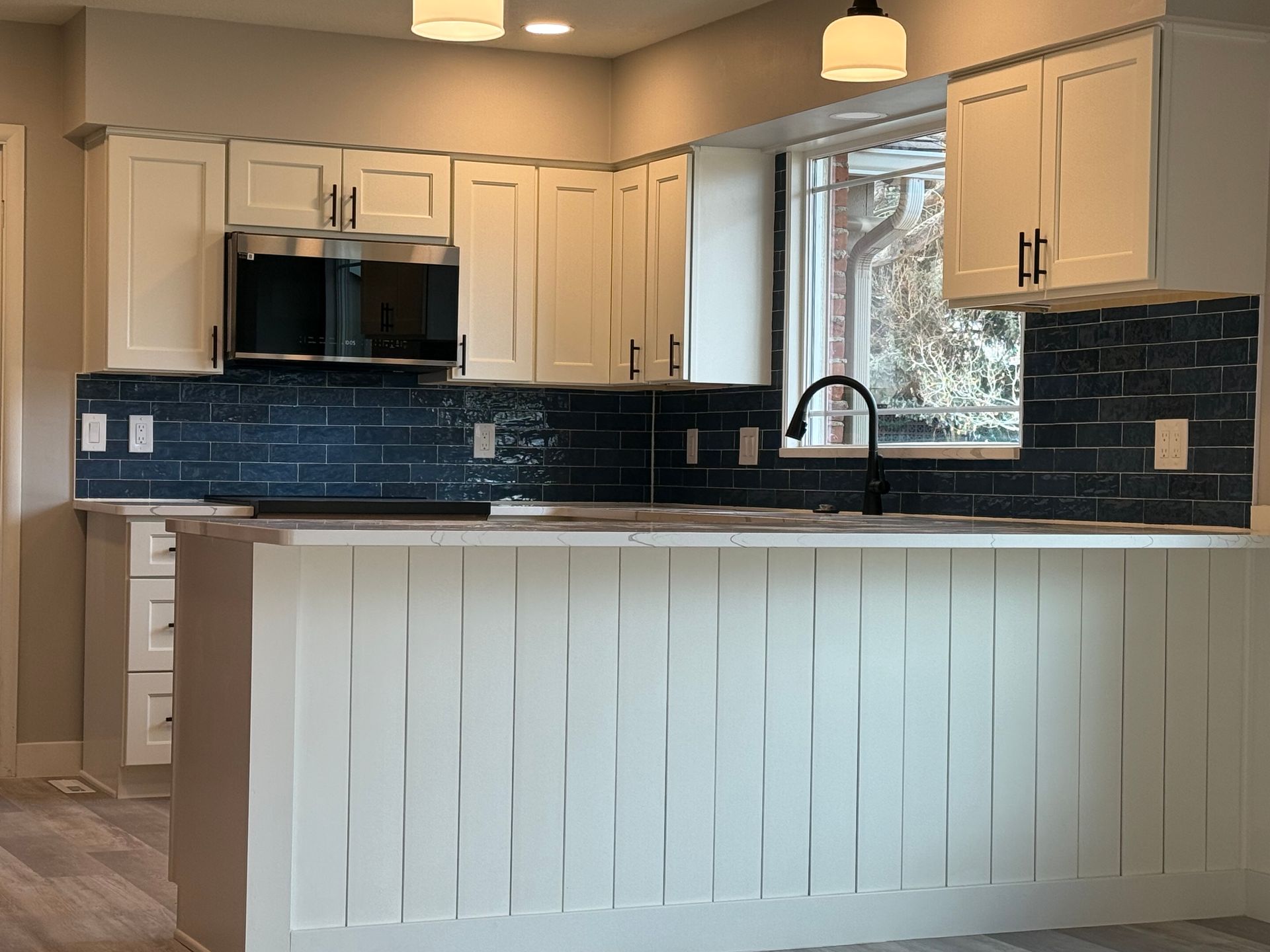 Kitchen with white cabinets, blue tile backsplash, and white island with vertical paneling.