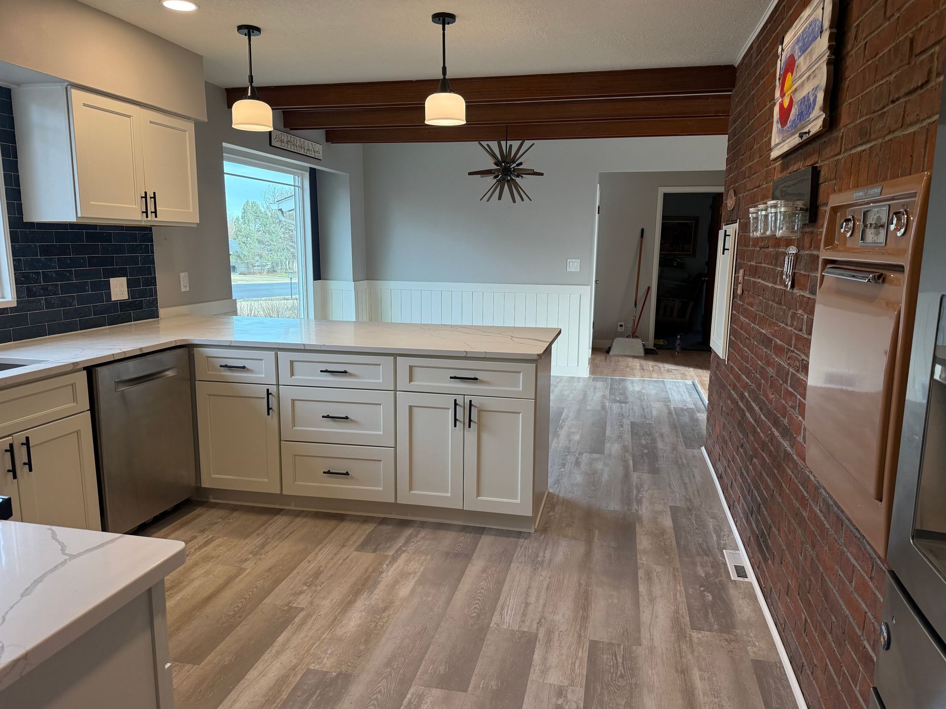 Newly renovated kitchen with white cabinets, wood-look flooring, and a brick accent wall.