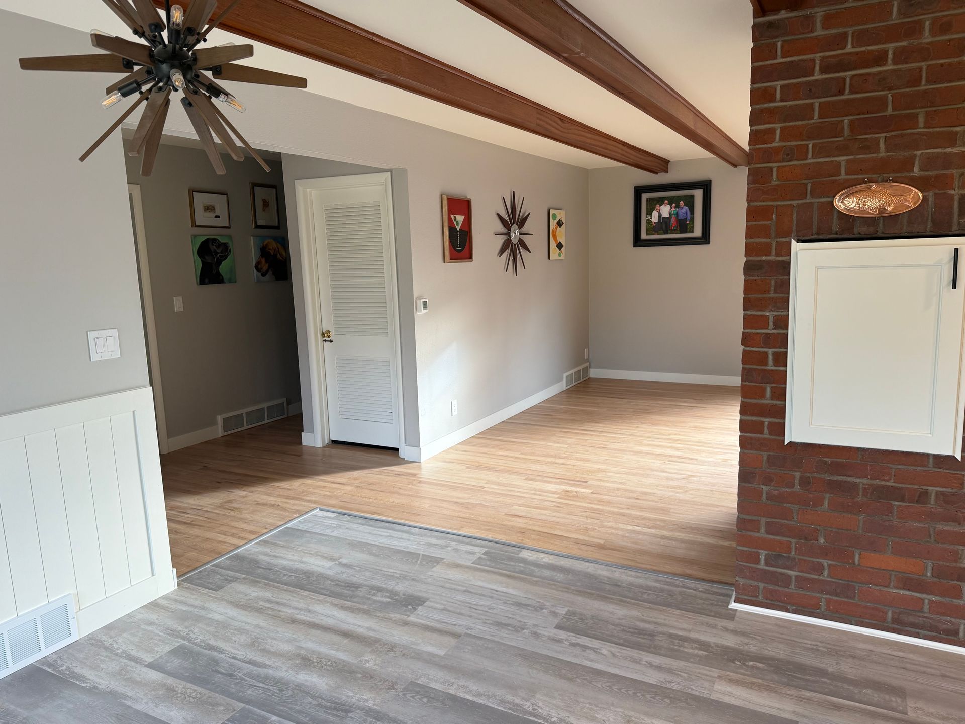 Interior room with exposed beams, brick wall, artwork, and various flooring types.