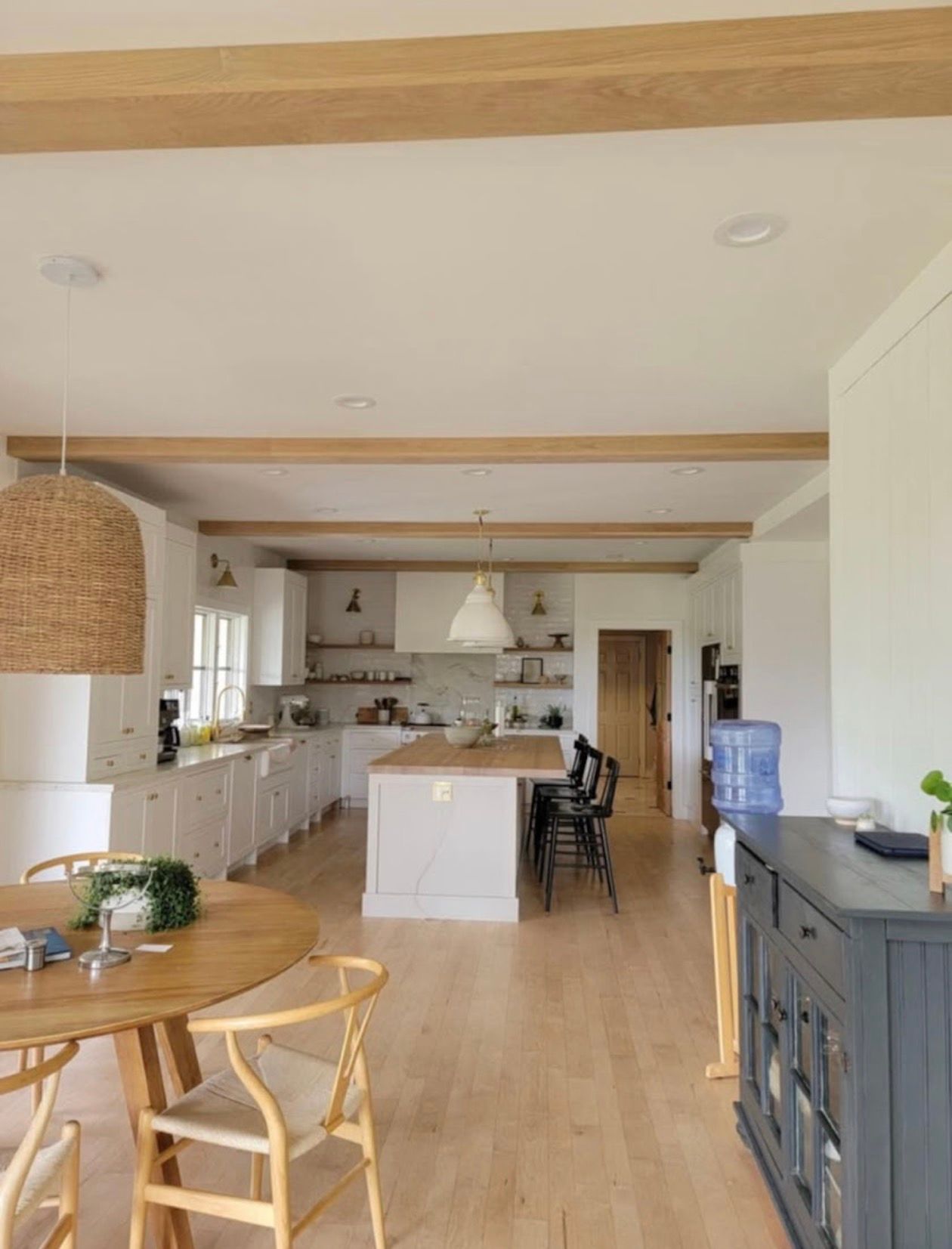 Bright, open kitchen with wooden beams. White cabinets, island, and dining area. Wooden floors and natural light.