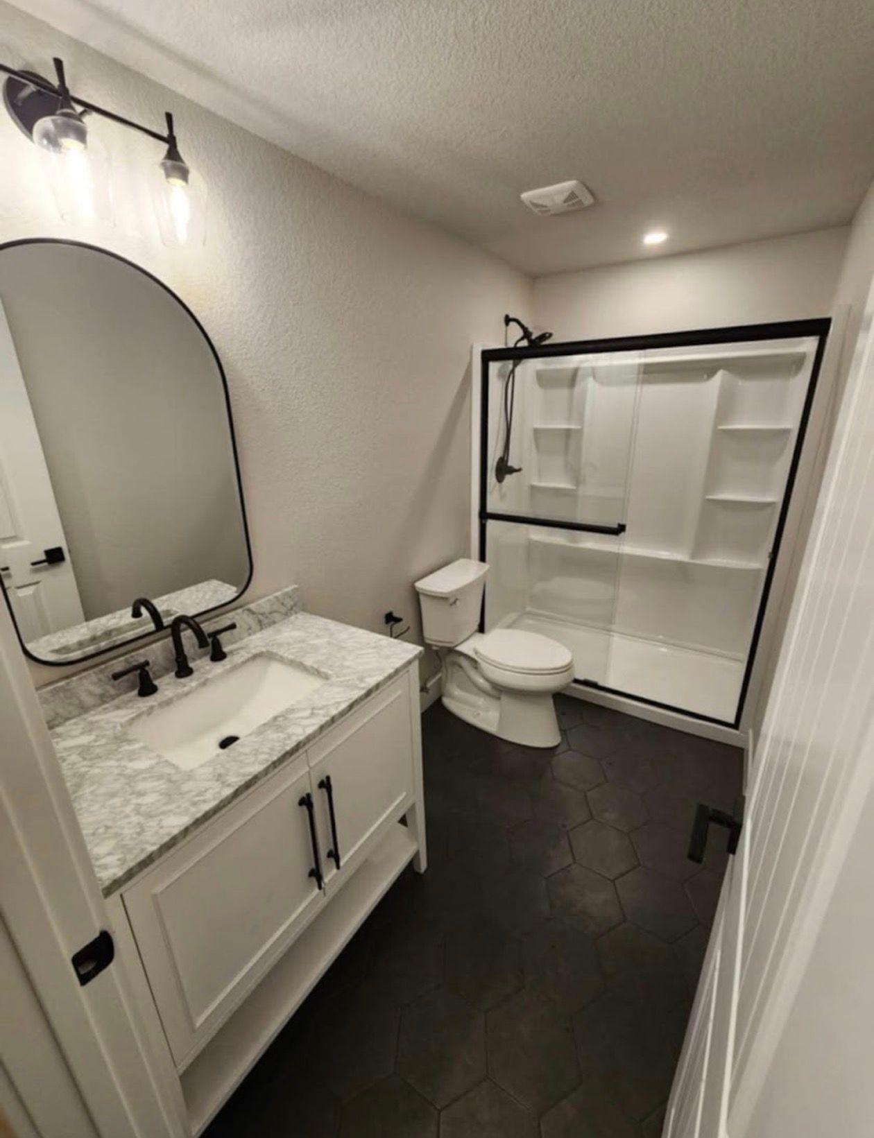 Bathroom with white vanity, black accents, and a shower stall. The floor is dark-colored tile.