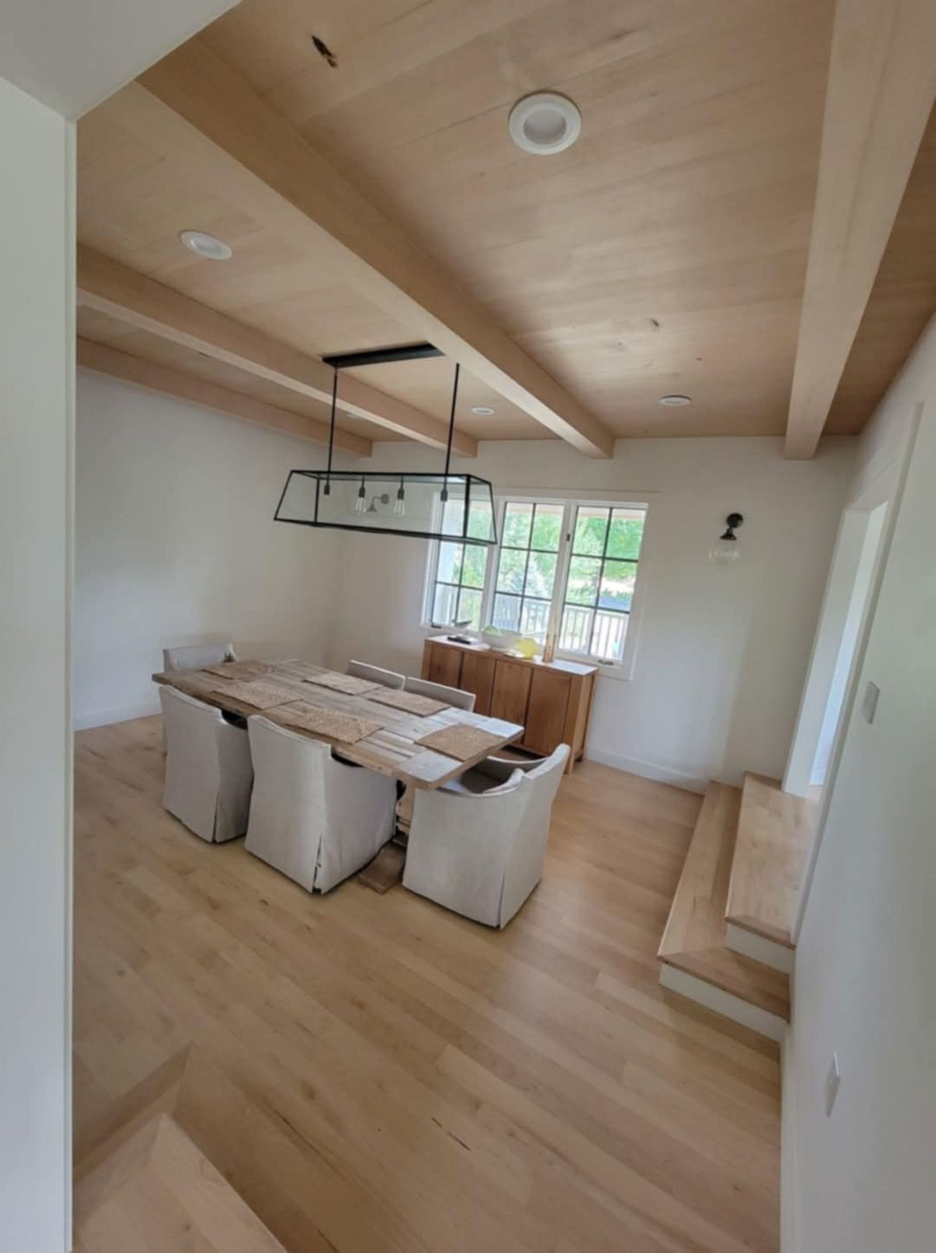 Dining room with light wood floors, table, chairs, beams, and windows.