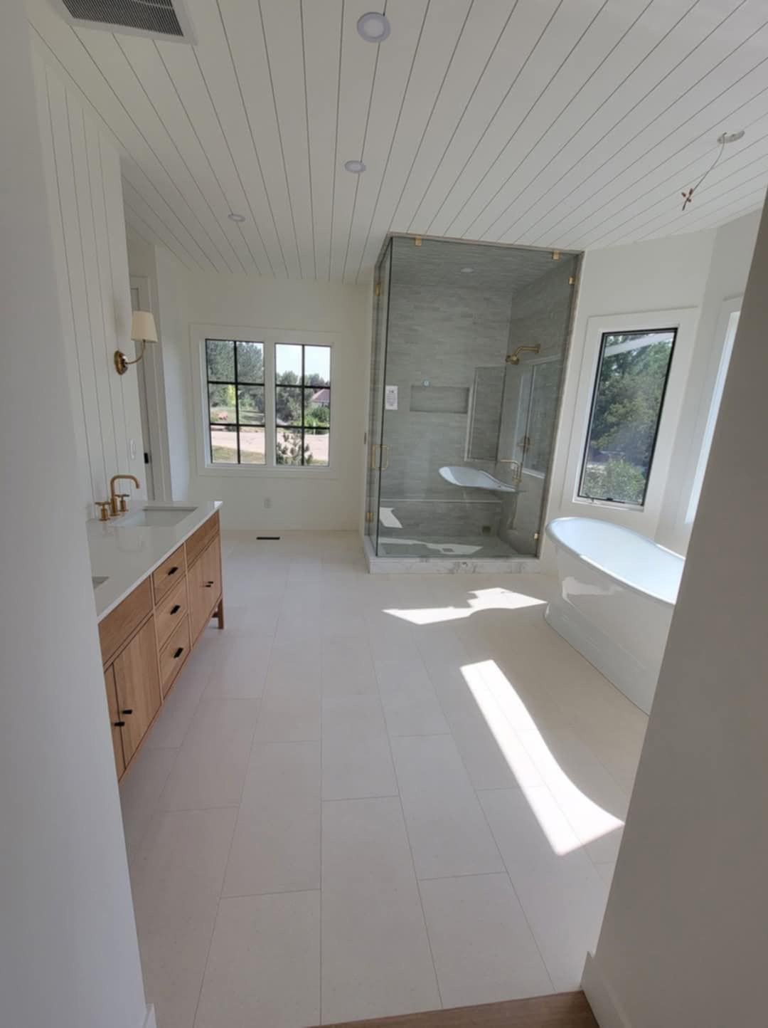 Spacious white bathroom with wood vanity, large shower, bathtub, and windows.