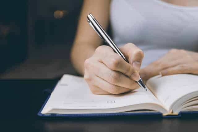 A woman is writing in a notebook with a pen.