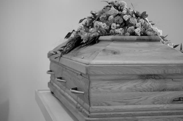 A black and white photo of a wooden coffin with flowers on top.