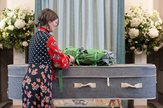 A woman is putting a green backpack into a coffin.