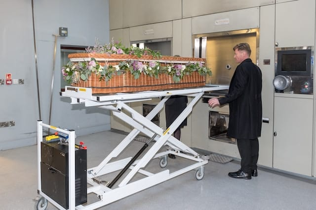 A man is standing next to a cart with a coffin on it.