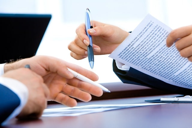 A person is holding a pen and pointing at a piece of paper.