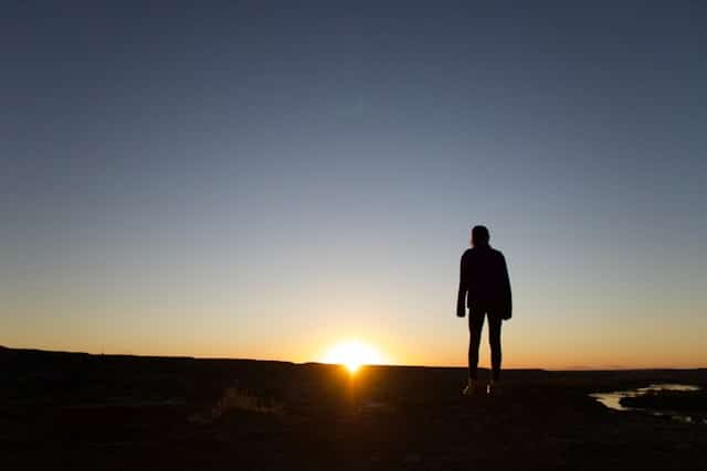 A silhouette of a person standing on top of a hill at sunset.