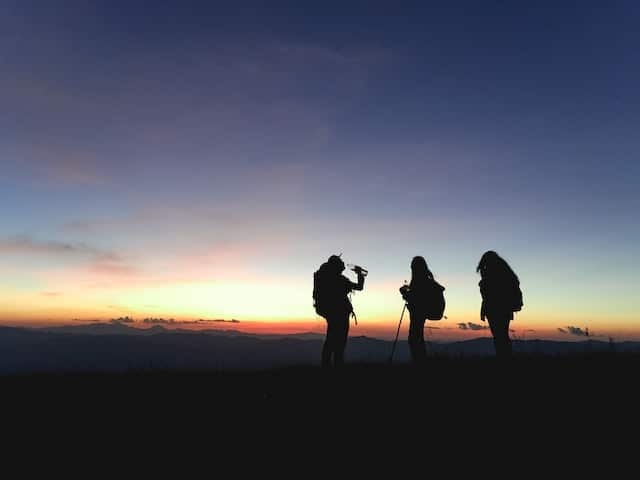 Three people standing on top of a hill at sunset