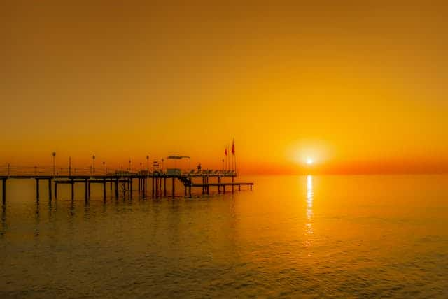 The sun is setting over the ocean with a pier in the foreground.