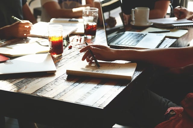 A group of people are sitting around a table with laptops and notebooks.