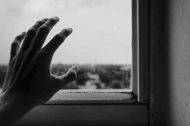 A person 's hand is reaching out of a window in a black and white photo.