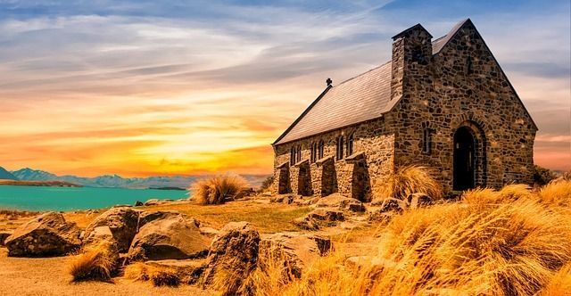 A small stone church sitting on top of a hill next to a body of water at sunset.