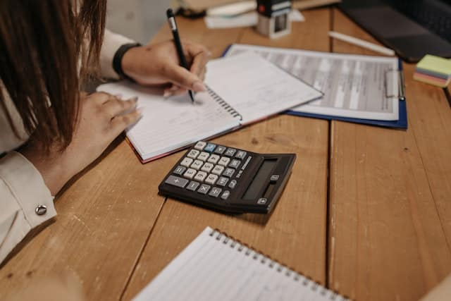 A woman is sitting at a table with a calculator and a notebook.