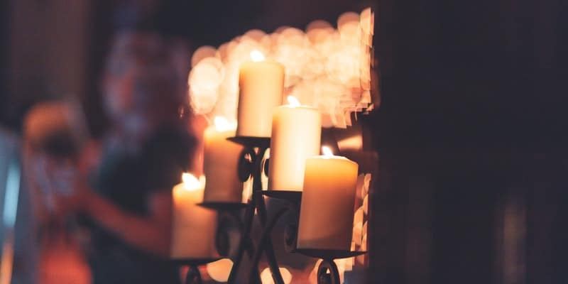 A man is standing in front of a candle holder filled with candles.