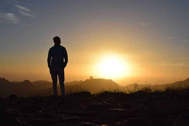 A man is standing on top of a hill at sunset.