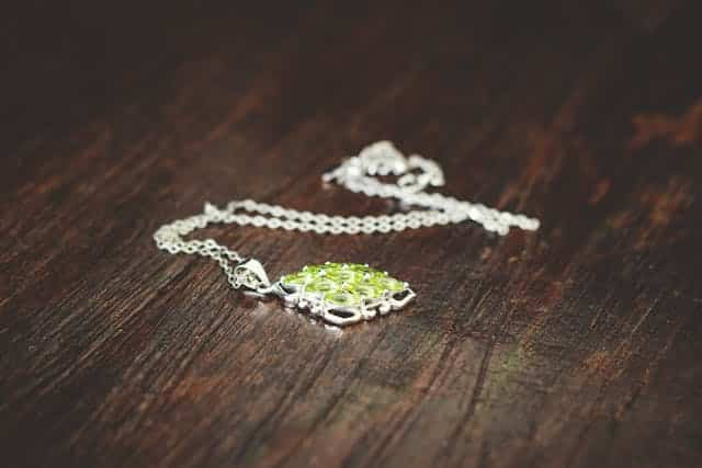 A necklace with a green stone is laying on a wooden table.