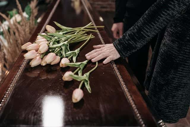 A woman is touching a coffin with flowers on it.