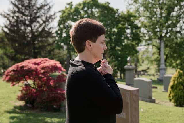 A woman in a black sweater is praying in a cemetery.