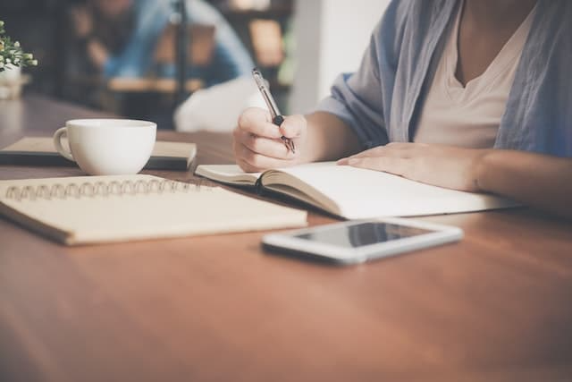 A woman is sitting at a table writing in a notebook.