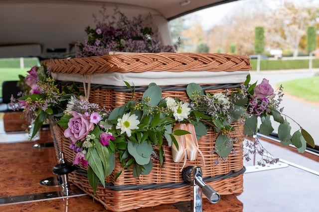 A wicker coffin decorated with flowers is in the back of a car.