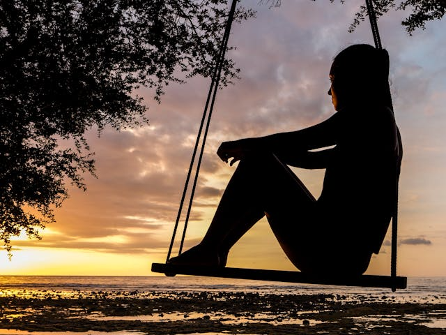 A silhouette of a woman sitting on a swing at sunset