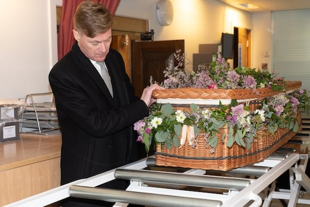 A man in a suit is arranging flowers on a coffin