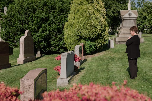 A man in a suit is standing in a cemetery looking at graves.