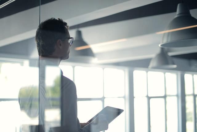 A man is standing in front of a glass wall holding a tablet.