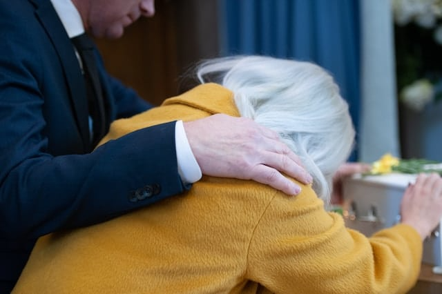 A man in a suit is hugging a woman in a yellow coat.