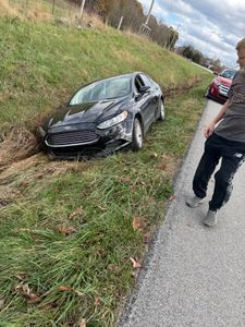 A car is sitting on the side of the road next to a grassy hill.