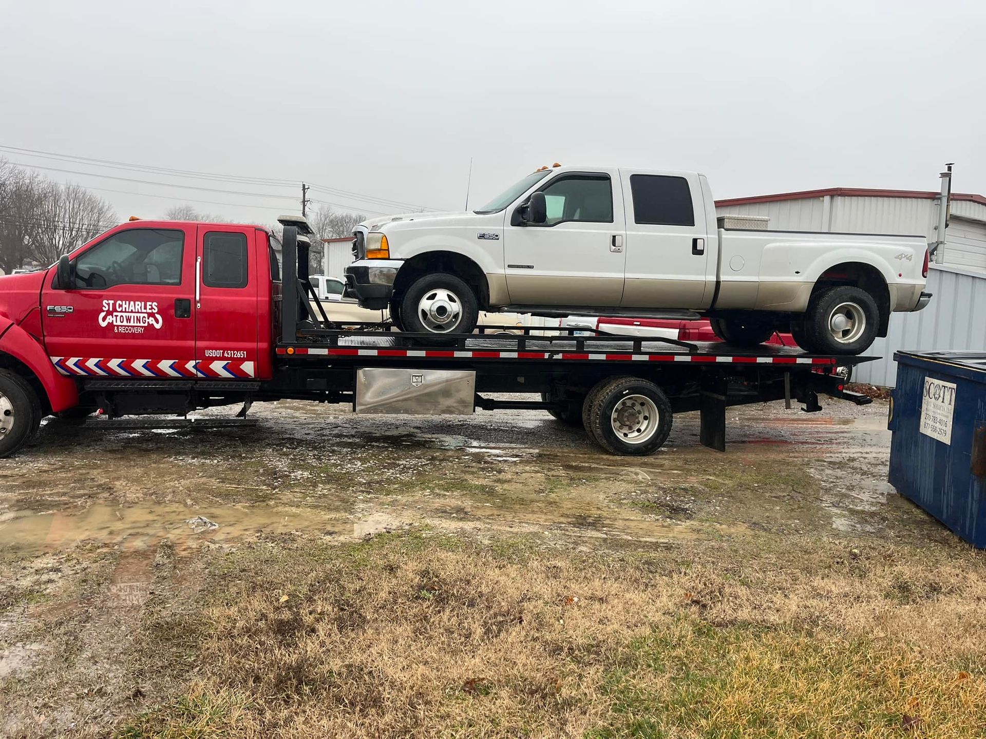 A red tow truck is towing a white truck.