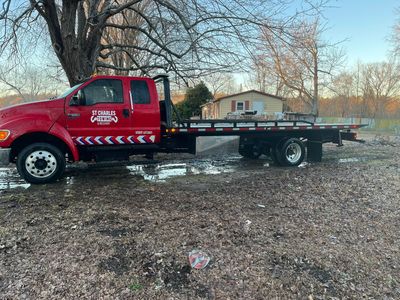 A red tow truck is parked in a field next to a tree.