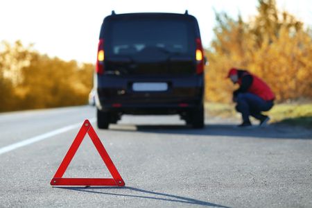 A man is kneeling next to a red triangle on the side of the road.