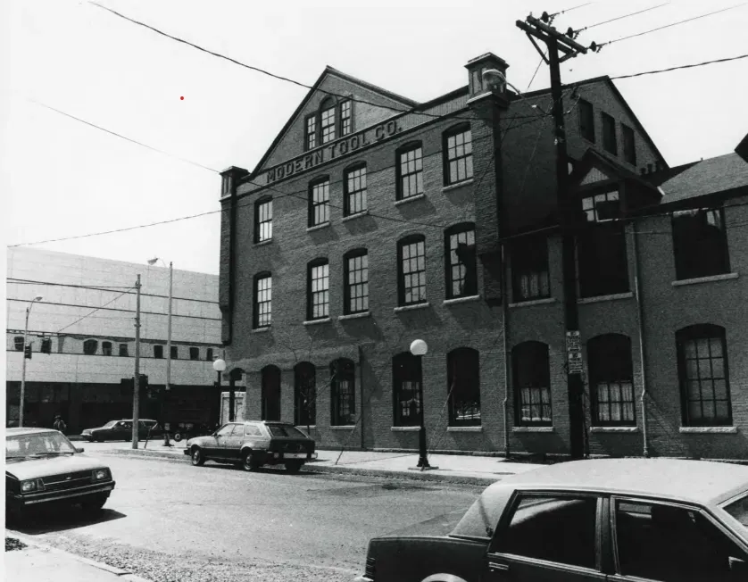 Brick building on a city street. Cars parked along the curb. 