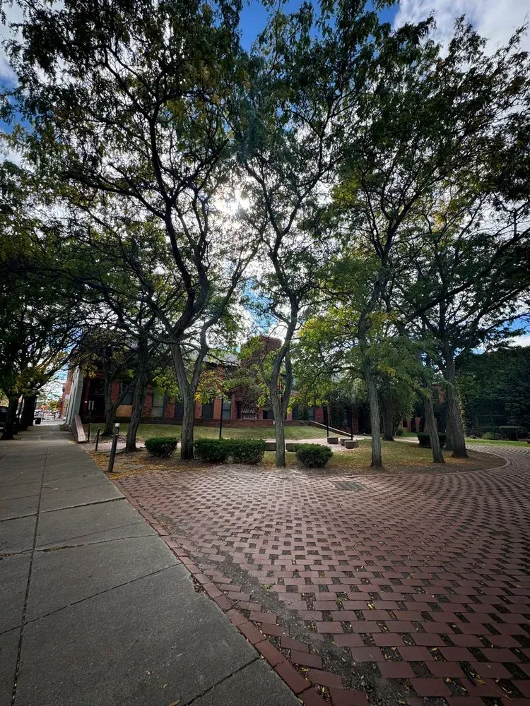 Brick path leading to a building framed by trees under a partly cloudy sky.