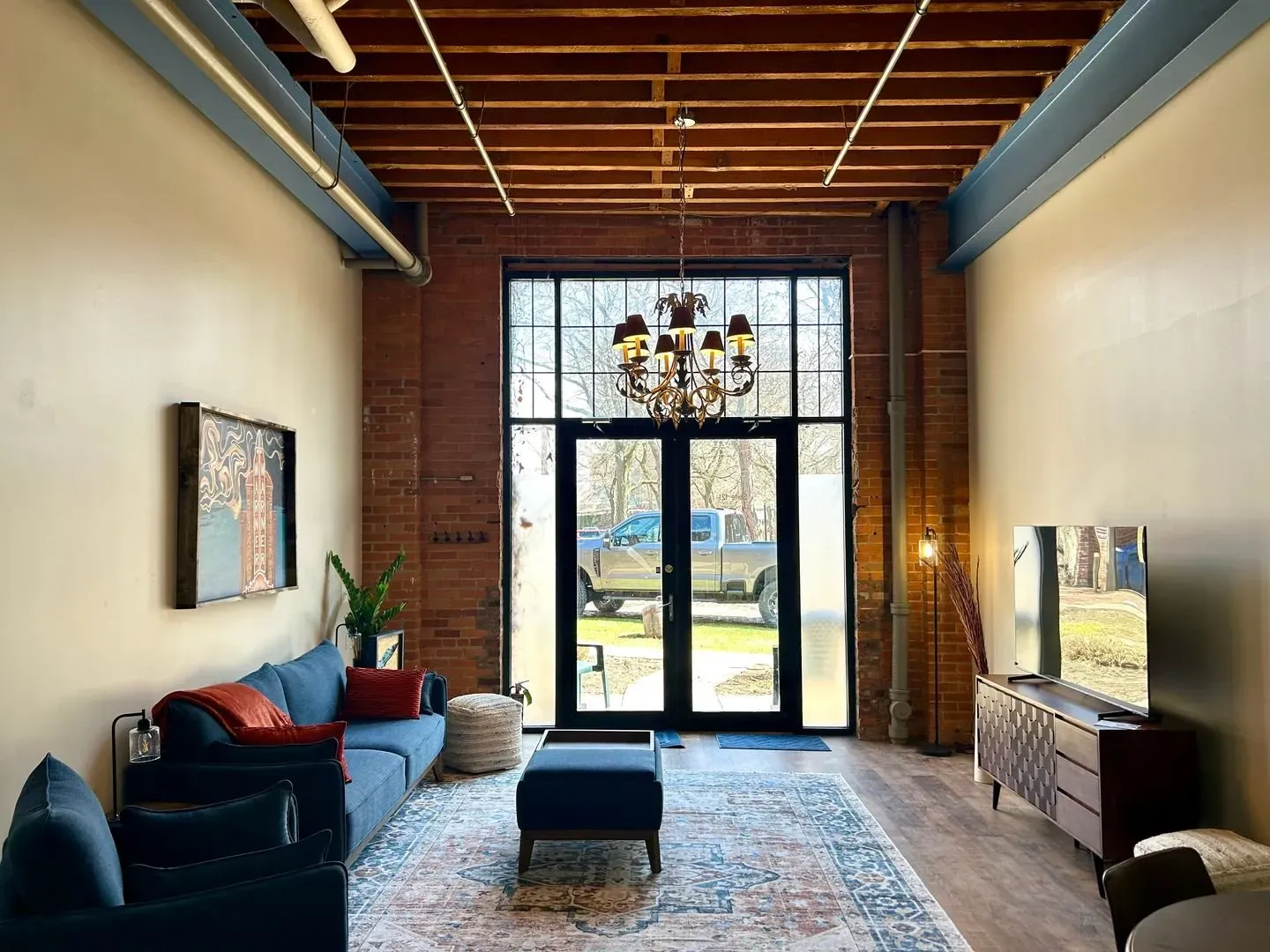 Living room with exposed brick, high ceilings, large windows, blue sofa, and rug.