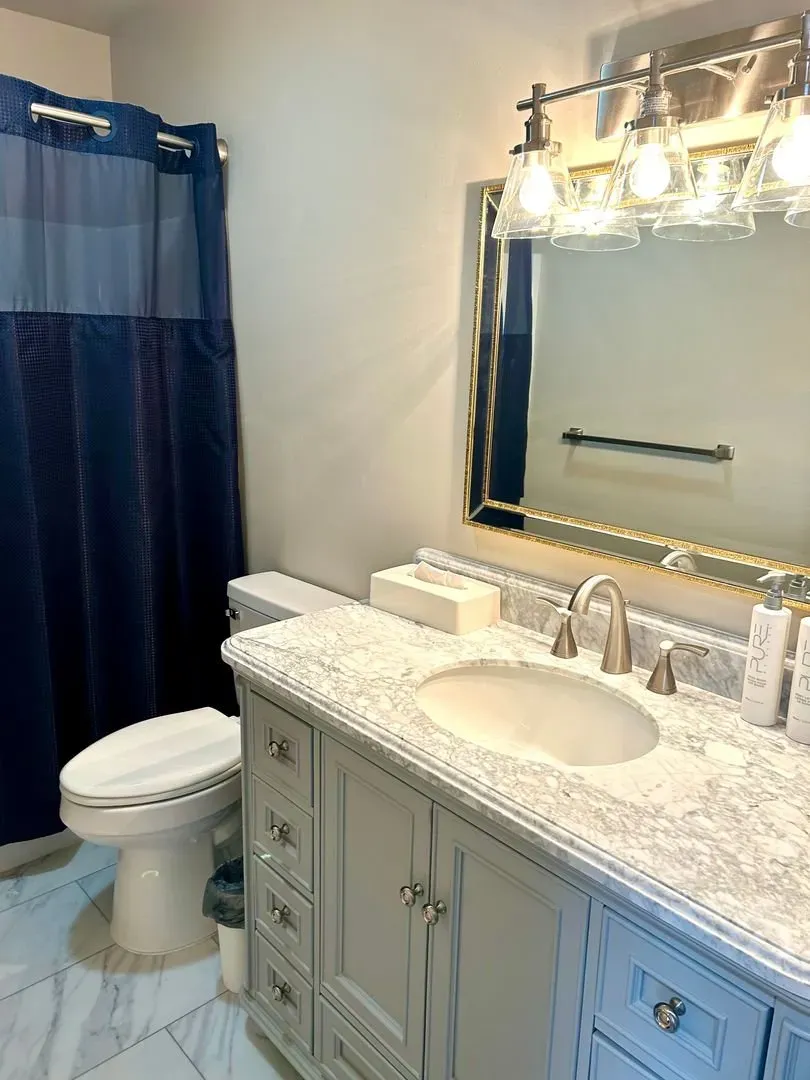 Bathroom with blue shower curtain, white vanity, and toilet.