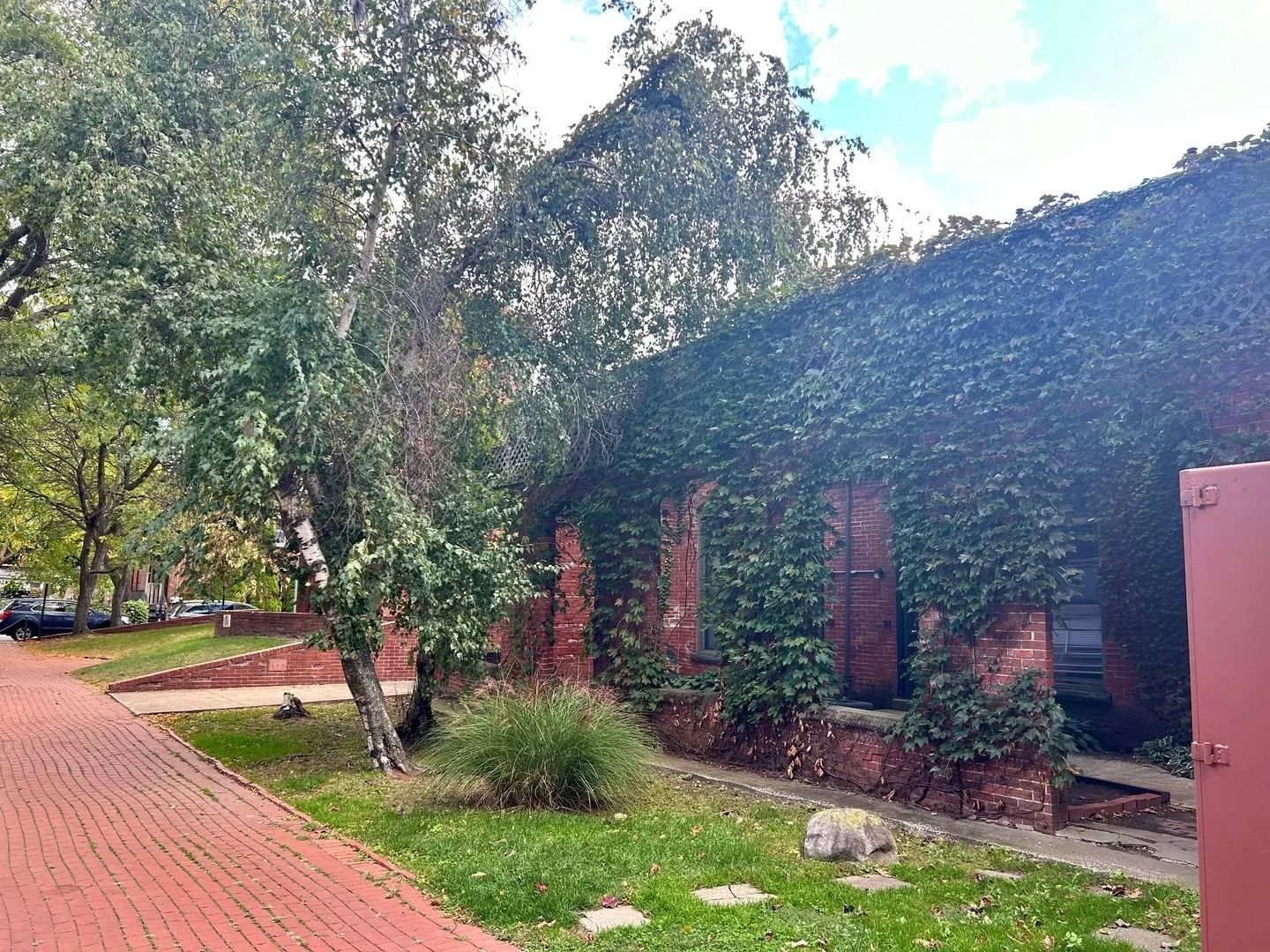 Red brick building covered in ivy, with a walkway and trees.