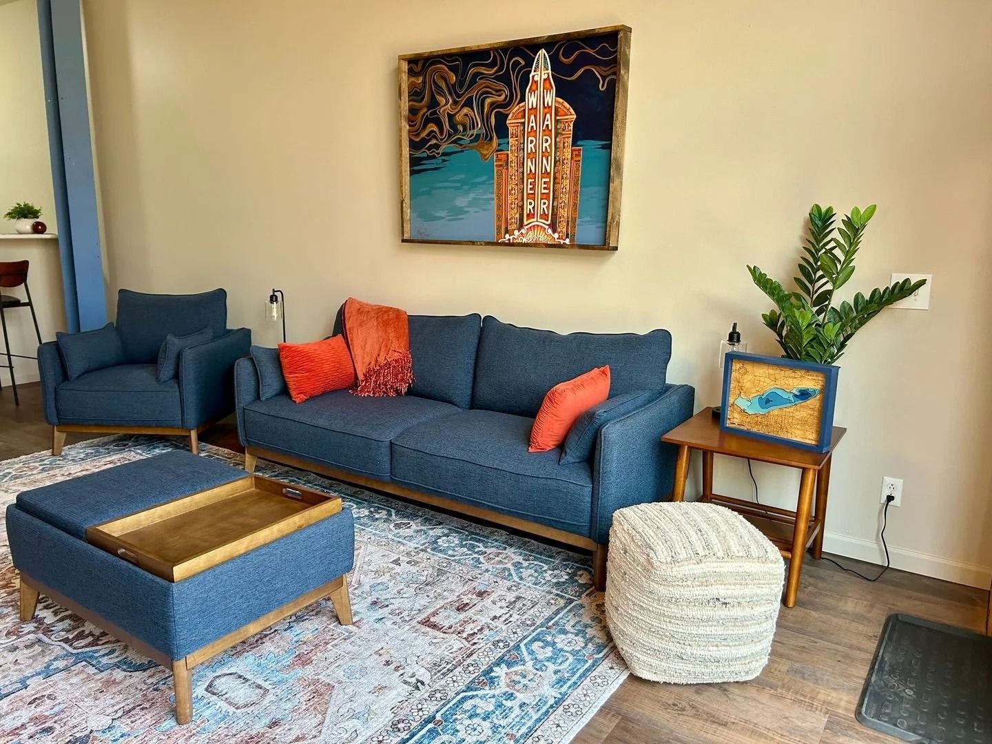 Cozy living room with blue furniture, orange pillows, rug, and artwork.