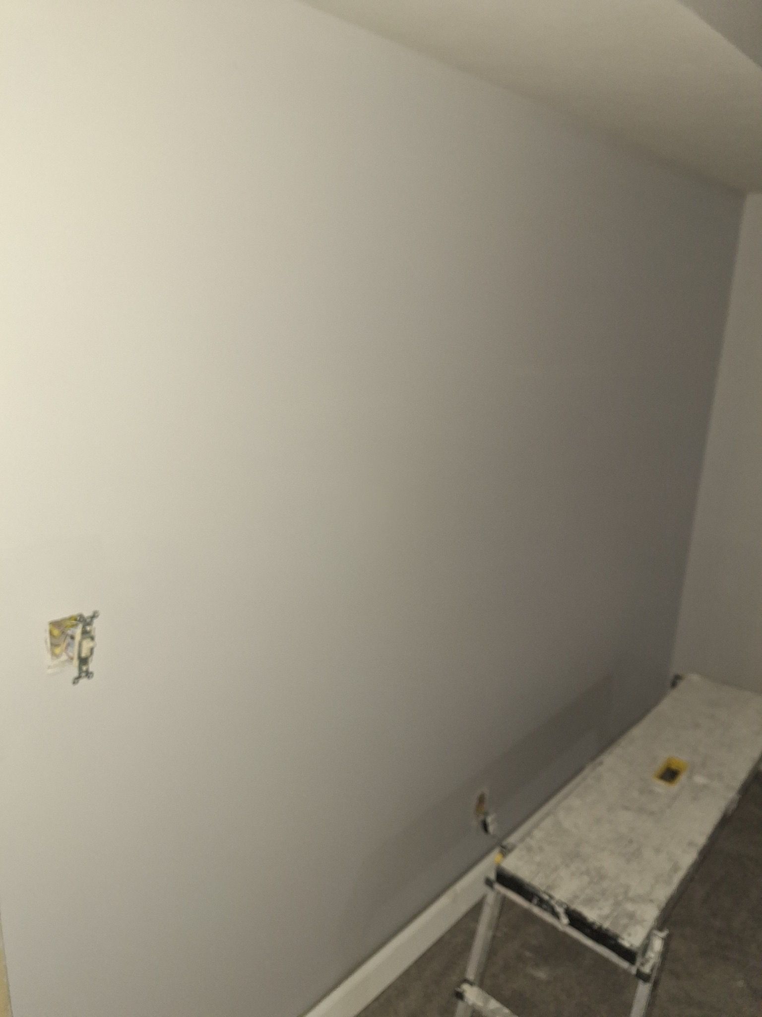 A freshly painted light gray wall in an interior room with a metal workbench in the foreground.