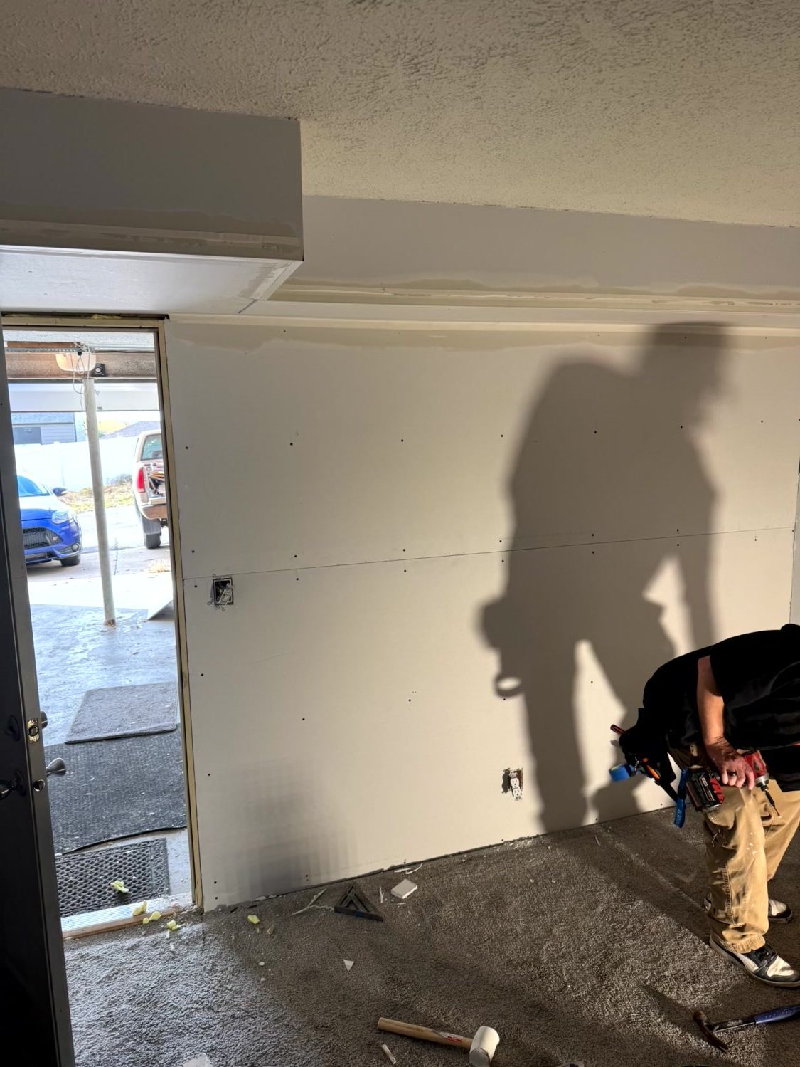 A person works on installing drywall in a room with a doorway visible to the left.
