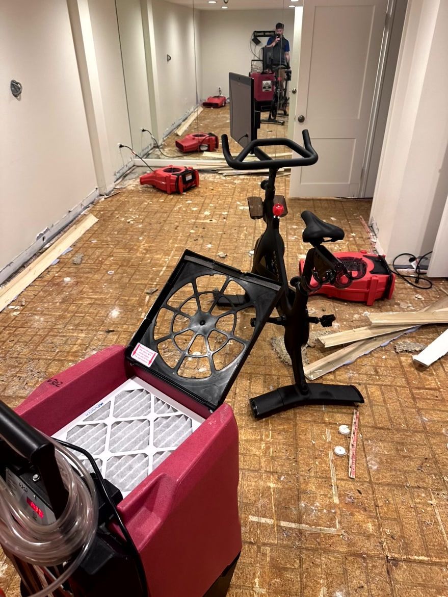 Industrial dehumidifiers and equipment sit on an exposed subfloor in a room undergoing water damage restoration.
